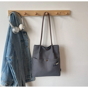 Detail of grey canvas tote bag featuring brown leather straps and character embroidery