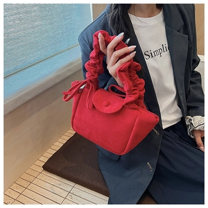 Close-up of red suede shoulder bag with pleated handle and retro flap design