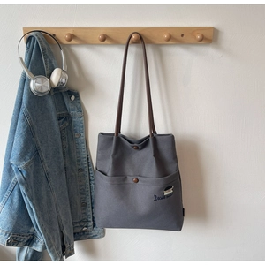 Detail of grey canvas tote bag with brown handles and embroidered pocket design