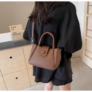Brown litchi leather bucket bag worn as a crossbody by a model in a minimal room