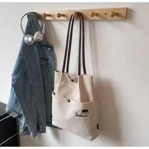 Detail of beige canvas tote bag with brown straps and Docile girl embroidery