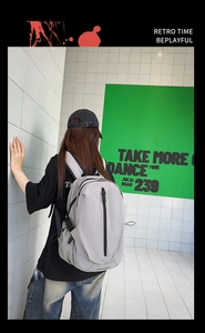 Rear view of a light grey nylon travel backpack with vertical zip pocket on a model