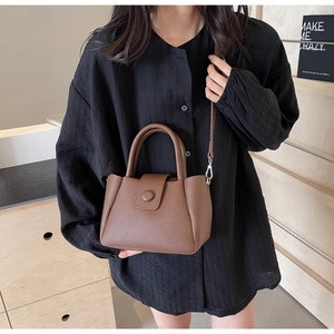 Detail of dark brown lychee leather handbag with circular clasp and smooth texture