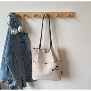 Detail of canvas tote bag with girl embroidery, brown leather strap, and metal snap button
