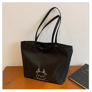 Detail of black canvas tote bag with golden reindeer embroidery on wooden desk