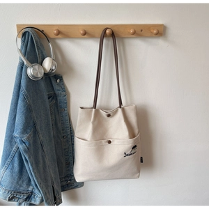 Close-up of cream canvas tote bag with brown strap and delicate character embroidery