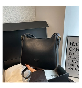 Detail of a minimalist black crescent leather bag with gold hardware in premium gift packaging