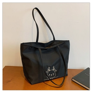 Detail shot of black tote bag with white elk embroidery on a wooden table surface