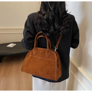 Détail d'un sac cabas en daim caramel avec poignées et finitions dorées porté par un mannequin