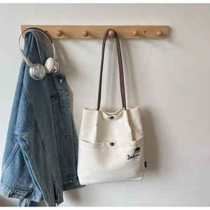 Detail of white canvas tote bag with Docile girl embroidery and brown button pockets