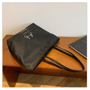 Close-up of black canvas tote bag with white deer embroidery on wooden stool