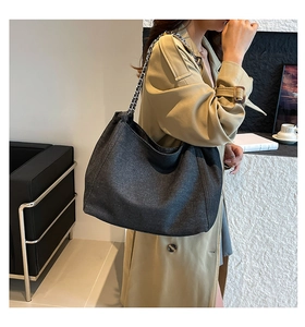 Detail der schwarzen Denim-Tote-Bag mit Silberkette, getragen zum beigefarbenen Mantel