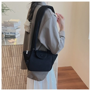 Side view of a black suede-textured pleated bucket bag worn by a model in a cozy room