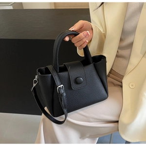 Close-up of black pebble leather tote bag with top handle and adjustable strap held by model