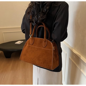 Sac à main trapèze en daim marron avec détails dorés porté par un mannequin en automne