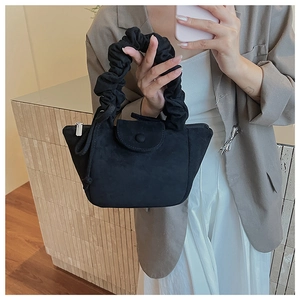 Detail of a black pleated handle bucket bag with a matte suede finish and metal buckle