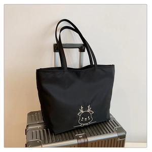 Close-up of black canvas tote bag with deer embroidery placed on a silver suitcase