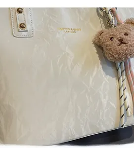 Detail of white pleated leather tote with gold studs and plush bear charm accent