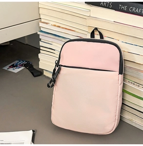 Rosa Mini-Umhängetasche mit Doppel-Reißverschluss und Schlaufe neben Büchern
