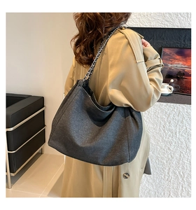 Detail of large denim tote bag with silver chain strap shown on model shoulder
