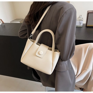 Detail of cream white leather bucket bag with textured finish on a dark suit