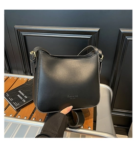 Detail of minimalist black leather bucket bag with gold lettering and adjustable strap