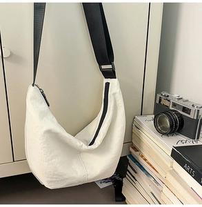 Minimalist white nylon crescent bag with black strap hanging against a neutral background