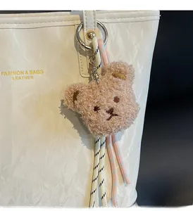 Close-up of a plush bear bag charm with beige texture and woven strap detail