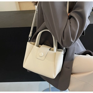 Détail du sac seau en cuir crème montrant la texture grainée et les poignées rondes