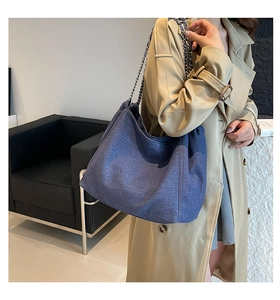 Detail of large dark blue denim tote bag with silver chain strap worn by a model