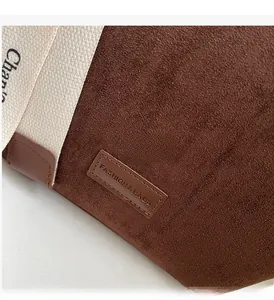 Detailed close-up of dark brown suede bag with cream canvas strap and leather brand label