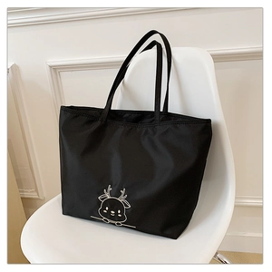 Detail of a black canvas tote bag with a minimalist deer pattern on a white chair