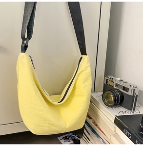 Detail of a yellow crescent nylon crossbody bag with black strap in a lifestyle setting