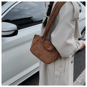 Detail of a brown suede pleated bucket bag worn as a shoulder bag against a white car