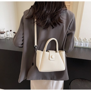 Detail of cream crossbody bucket bag with pebble leather texture on a grey suit jacket