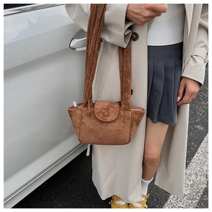 Detail of a brown suede bucket bag featuring a wide shoulder strap and textured finish