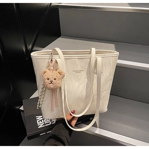 Close-up of white marble pattern tote bag with teddy bear charm on leather strap