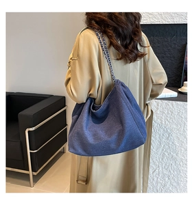 Detail of large denim tote bag with silver chain strap shown in a modern interior setting
