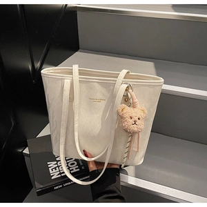 Close-up of white leather tote bag with gold lettering and cute bear plush charm accessory