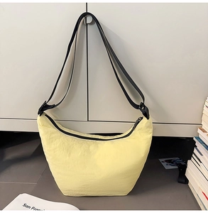 Detail view of a pale yellow crescent bag with crinkled texture and black strap