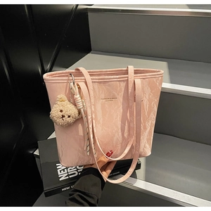 Close-up of pink pleated tote bag with plush bear charm and striped woven accessory