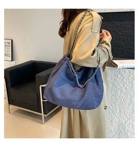 Detail of blue denim tote bag with metal chain strap shown on model shoulder