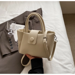 Détail d'un sac cabas en cuir grainé beige avec fermeture à bouton et bandoulière