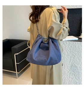 Detail of blue denim tote bag with chain strap worn over a khaki trench coat