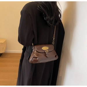 Detail view of deep brown vintage leather shoulder bag with gold oval buckle and glossy finish