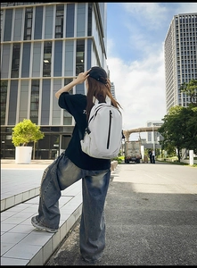 Close-up of white lightweight travel backpack with black zipper pocket and brand logo