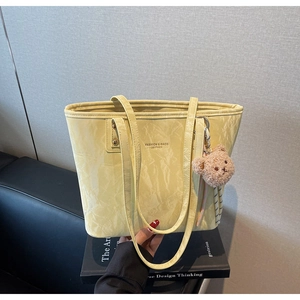 Detail of light yellow pleated leather tote bag with plush bear charm and text