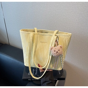 Close-up of pale yellow tote bag with pleated texture and a cute brown bear charm