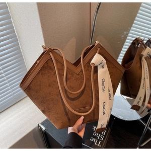Detail of a brown suede tote bag with a unique V-shaped opening and lettered strap