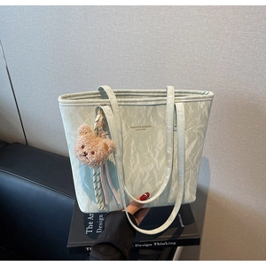 Detail of mint green pleated tote bag featuring brown teddy bear charm and soft long straps